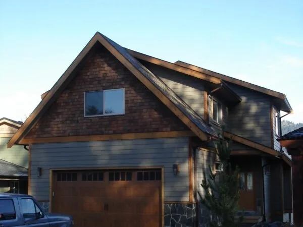 Two-story house with brown garage doors and stone exterior under clear sky.