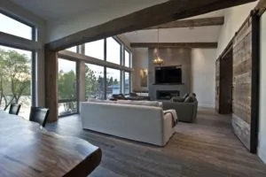 Modern living room with exposed wooden beams, fireplace, and large windows overlooking a lake.