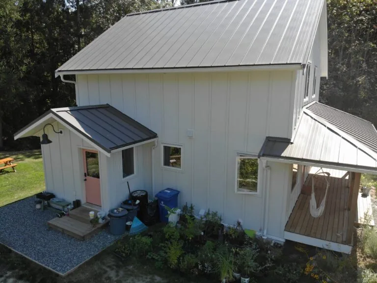 White metal-roofed residential building with covered entry porch, surrounded by gravel landscaping and trees.