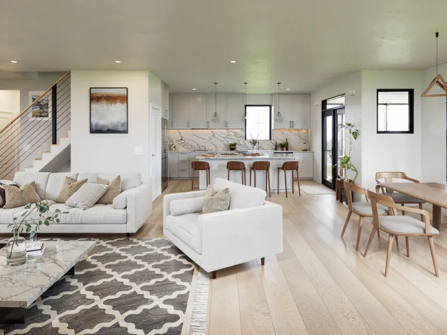 Open-concept modern home interior with white seating, kitchen with marble backsplash, wooden dining table, and light wood flooring throughout. (3 of 5)