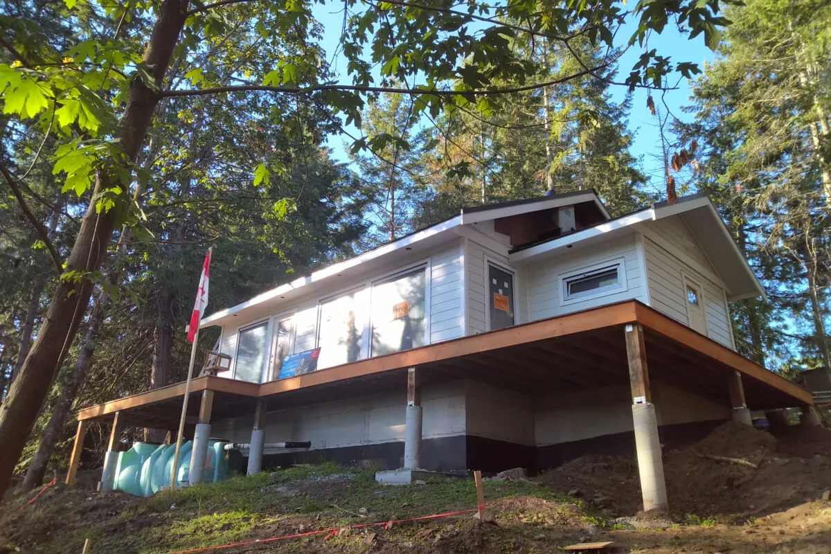 Modern elevated house nestled among tall trees with wooden deck and white siding.