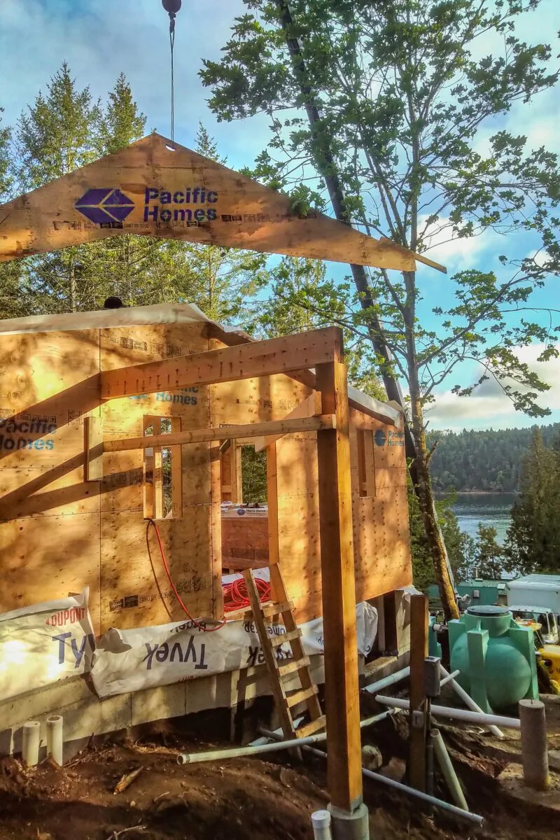 Pacific Homes construction frame under crane near waterfront with forested mountains and lake visible.