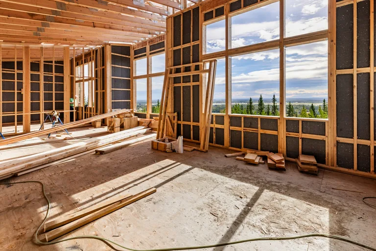 Interior of a house under construction with wooden window frames and mountain views through large windows.
